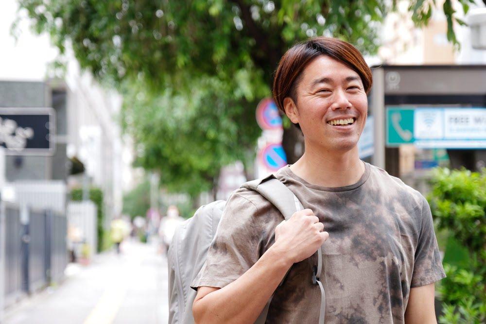 Tシャツ姿でリュックを持つ小山トレーナー