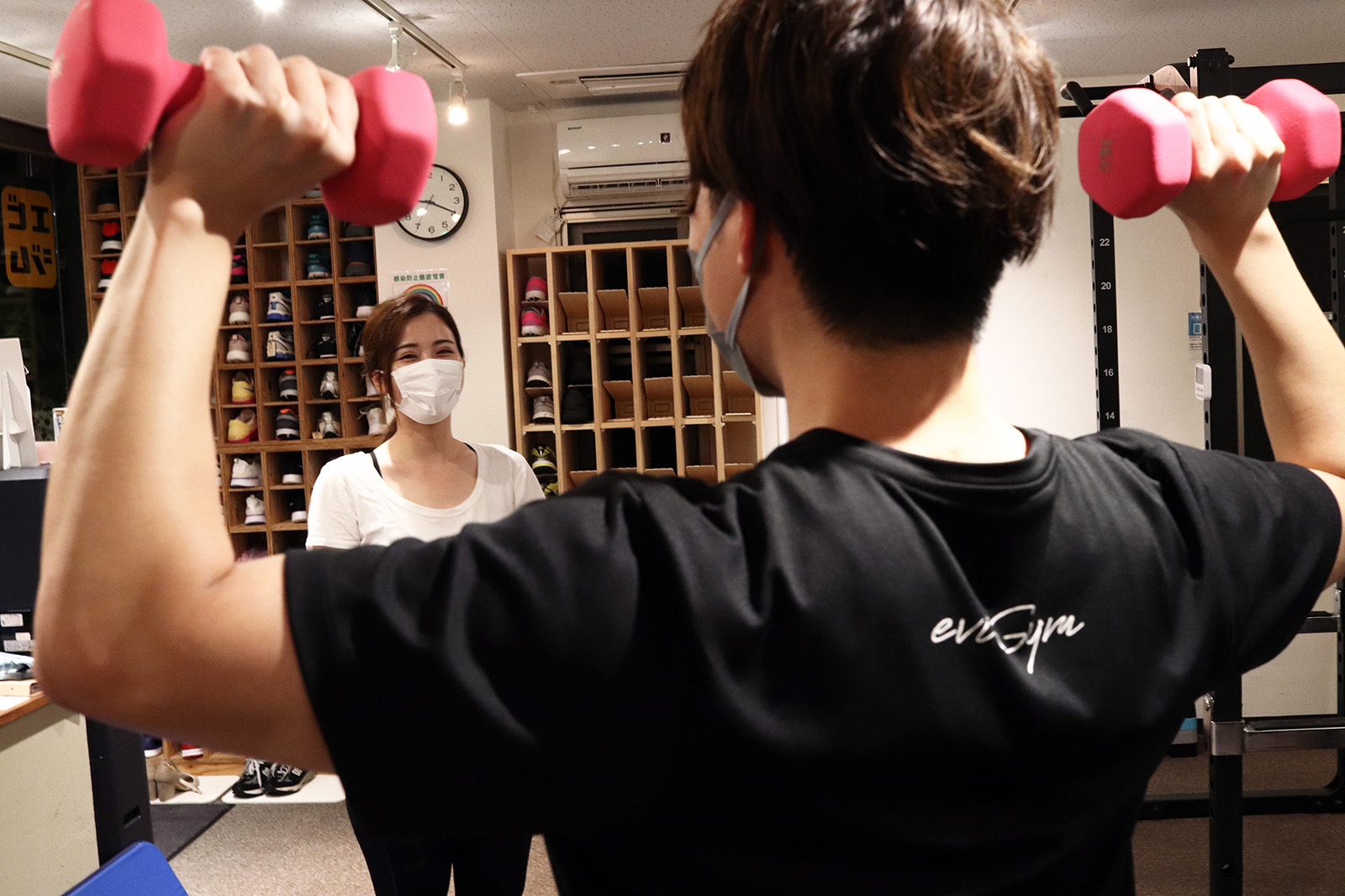 ダンベルを両手に持つトレーナーを見ているお客様